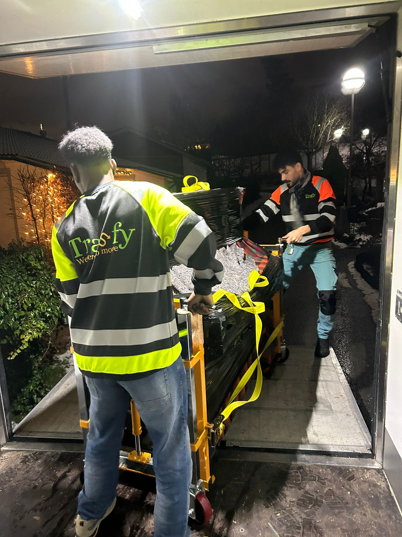 Två flyttare från Trasfy rullar in ett inplastat piano i flyttbilen