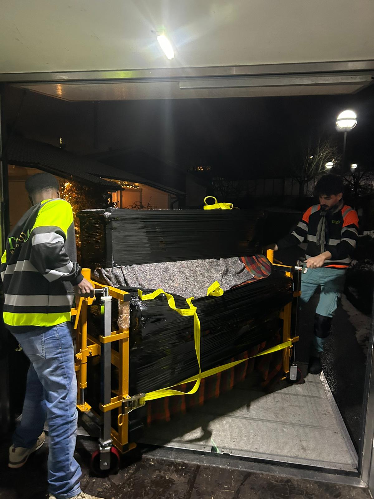Ett inplastat piano surrat på pianovagn vid flyttbilens öppning